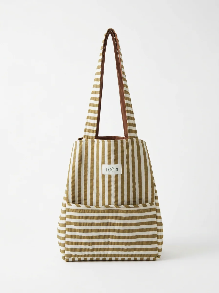 Bolso LOÖRI de rayas camel y crudo colgado sobre pared clara
