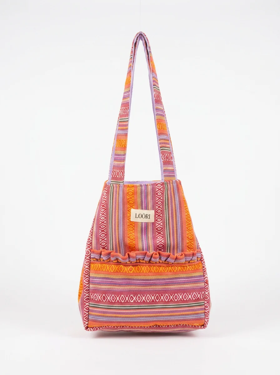 Bolso LOÖRI CARMELA de tela de aguayo en tonos rosas, corales y naranjas sobre fondo blanco
