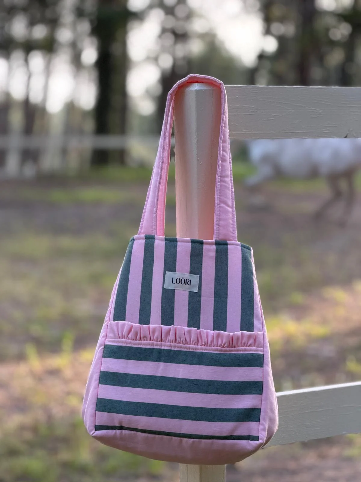 Bolso LOÖRI de rayas rosa y verde colgado de una valla blanca